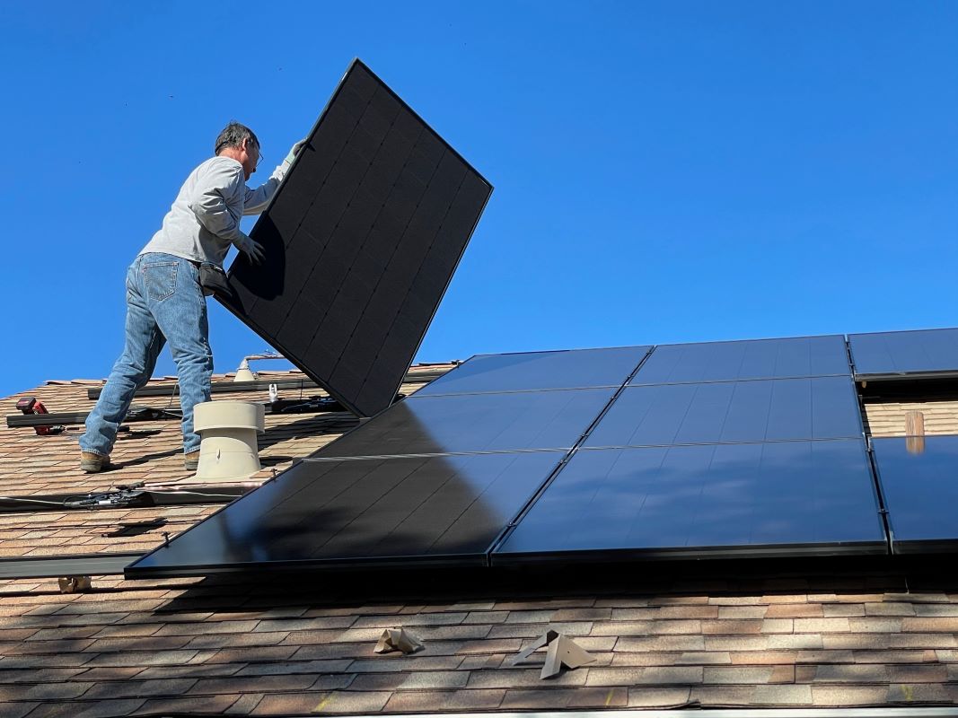 Combien coûte un panneau solaire. Un homme sur un toit installe un panneau solaire
